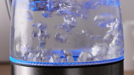 Bubbles in hot water boiling inside glass teapot in bright sunlight on the kitchen. Close-up of boiling water in transparent kettle.