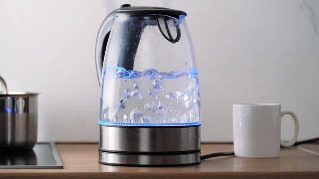 Bubbles in hot water boiling inside glass teapot in bright sunlight on the kitchen. Close-up of boiling water in transparent kettle.