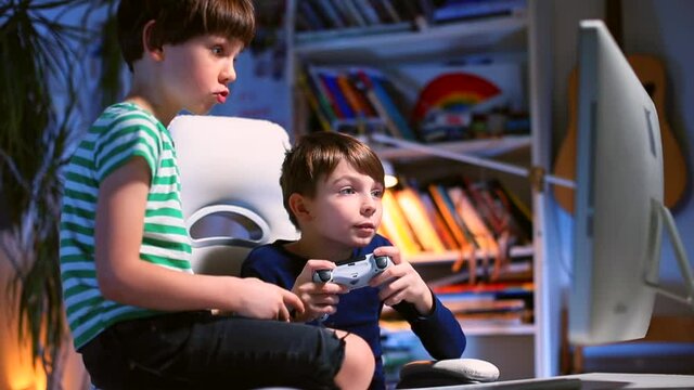 Evening room teenagers use joysticks to control the game ps4 at the table. Focus on the monitor. Emotional exchange using electronic devices. Camera movement.