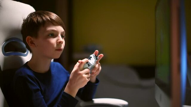 He holds the controller of an electronic game ps4 in his hands. Concentration of attention to the monitor. Emotions in game. Smart boy is playing a video game using a monitor. 