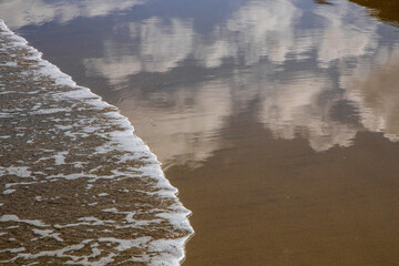 Abstract painterly image of clouds reflected in wet sand at a beach