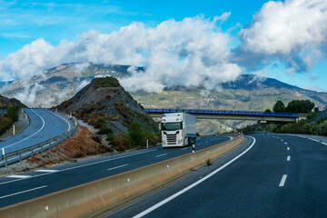 Truck with refrigerated semi-trailer driving on the highway and with a landscape of mountains and...