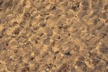 the water swirls and forms a texture through which you can see yellow sand and small stones