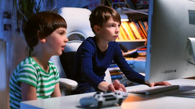 Evening room. Teenagers use the computer in the evening at the table. The boy is typing text on the keyboard. Search for information on the Internet. Focus on the monitor.
