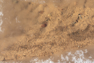 the water swirls and forms a texture through which you can see yellow sand and small stones