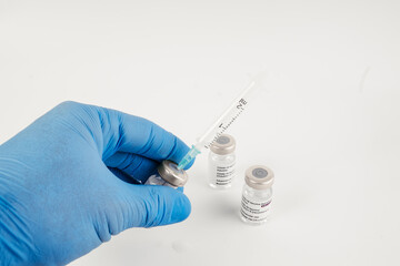 Blue gloves with three Covid-19 vaccine vials with white background and a syringe to inject medical professionals and people at risk.. SARS-CoV-2 vaccination treatment. Copy space.