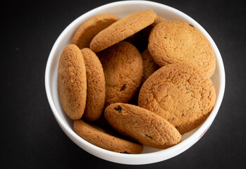 Oatmeal cookies in a white bowl on a black background. 