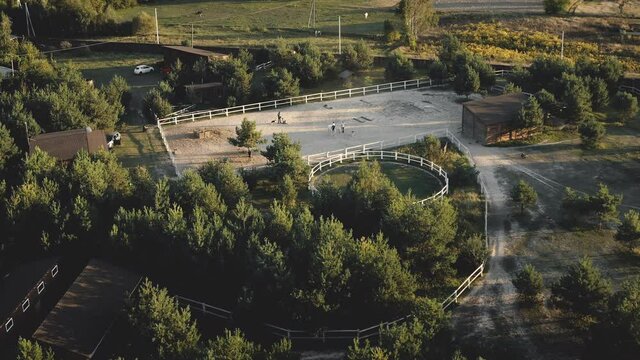 Racecourse at ranch aerial. Horseback woman training. Trainer teach girl ride on horse. Equestrian sport. Autumn nature landscape. Green grass valley, trees at sun day. Recreation countryside vacation