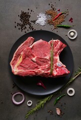 Raw beef steak with various herbs and spices on a dark background. View from the top.