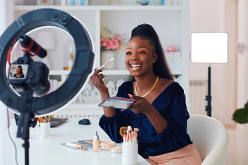 happy young african american woman streaming a beauty vlog from home, online content creator applying a makeup on - 411342745