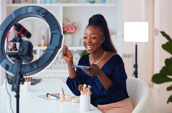 happy young african american woman streaming a beauty vlog from home, online content creator applying a makeup on