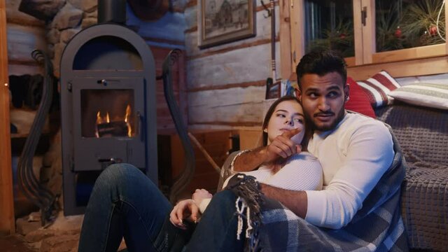 Lazy winter days. Young couple enjoying winter holidays. Hugging and speaking near the fireplace. High quality 4k footage