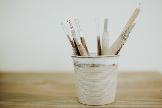 Tools of a craftsman (craft tools) in a ceramic cup, in a clear and white environment on a wooden table