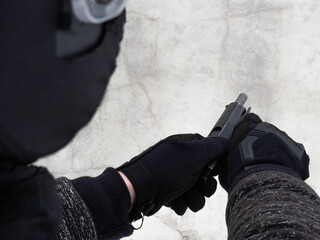 A man wearing black tactical gloves and a Russian assault helmet with a visor, holds and reloads a...