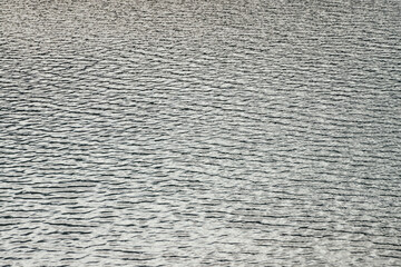 Monochrome texture of silver calm water of lake. Meditative ripples on water surface. Nature minimal background of gray lake. Natural black white backdrop of clear water. Lake fragment in grayscale.