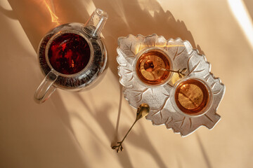 Teapot and glasses of tea on a leaf-shaped tray. Breakfast on the Solcie Morning. Hard shadows on a beige background.  
Close-up top view