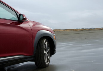 Fototapeta na wymiar Red hatchback riding on sandy beach in Ocean Shores
