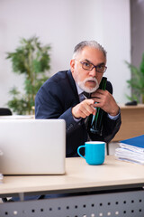 Old male employee drinking alcohol in the office