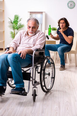 Fototapeta na wymiar Old man in wheel-chair and young bad caregiver indoors