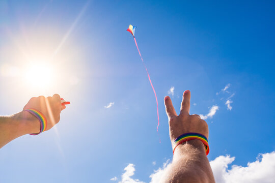 close up and portrait of arms and hands up wearing bracelet of lgtb colors and flying a kite in the sky