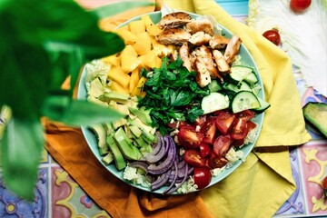 Homemade paleo salad with grilled chicken meat, mango, fruits and veggies ingredients, top view.