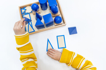 Top view of girls hand is sorting a puzzle of colored wooden geometric shapes in montessori school.