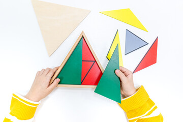 Top view of girls hand is sorting a puzzle of colored wooden geometric shapes in montessori school.