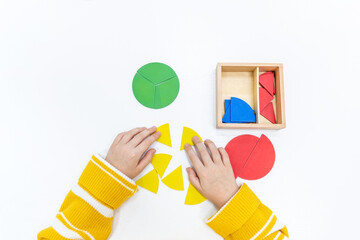Top view of girls hand is sorting a puzzle of colored wooden geometric shapes in montessori school.
