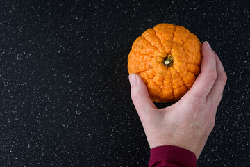 Woman’s hand putting down a fresh large orange with wrinkled and textured skin on a black cutting...