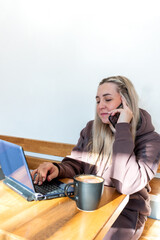 Young woman in a comfortable tracksuit works on the computer and talking on mobile phone.