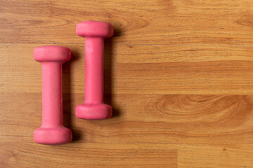 Fototapeta na wymiar Pair of pink dumbbells on wooden floor for indoor training. Sports equipment for a person with a fitness lifestyle.