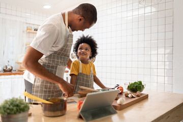 Black African American Father and son doing online cooking with digital tablet in kitchen