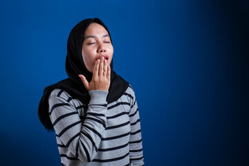 Asian muslim woman wearing hijab yawning tired, dizzy expression
