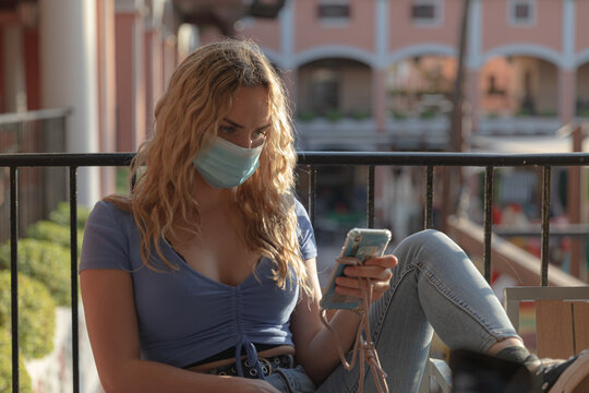 joven rubia esperando pacientemente con el m&oacute;vil c&oacute;modamente sentada con camisa azul vaqueros y converse.