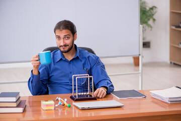Young male teacher physicist sitting in the classroom