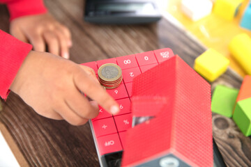 A calculator and a model of a small house and a pair of small hands that are putting euro coins on the calculator