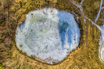Round shape of a frozen lake as a top shot from a drone, looking down to a beautiful peace of a winter landscape.