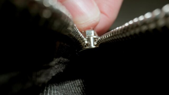 MACRO: Human hand unzips the clothes zipper