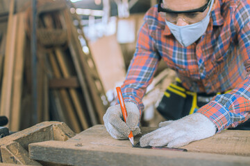 carpenter is working in a woodworking office.caucasion white Carpenter using tape measure to measure distance and marking with pencil