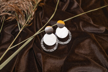 Closeup of trendy round earrings with mother of pearl and plastic elements on crumpled brown silk...