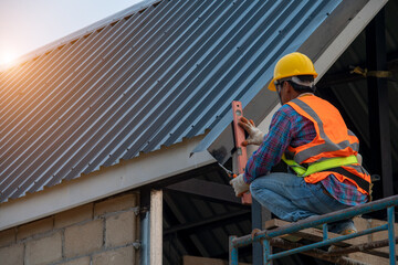 Roofer working on roof structure,Roofer installing Metal Sheet on top roof. © visoot