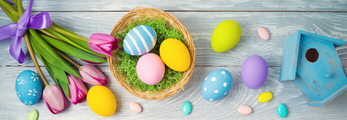 Naklejka premium Easter holiday concept with easter eggs in basket and tulip flowers on wooden background