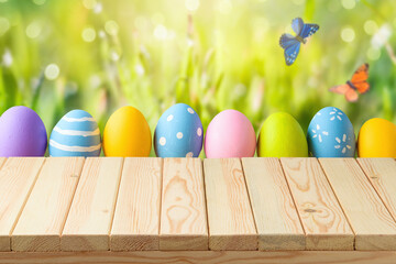 Easter holiday background with empty wooden table and Easter eggs over green grass meadow