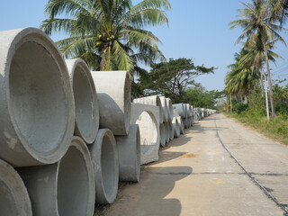 Concrete sewer pipes are stacked at construction site on roadside in Thailand, Road with coconut...