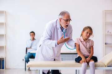 Small girl with her father visiting old male doctor