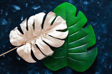 golden and green artificial monstera leaves on blue background, concept of luxury vs simpler products