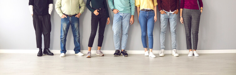 Your shoes says a lot about you. Cropped image of the legs of people in ordinary clothes and shoes standing in a row near the wall. Concept of diverse people in modern business. - obrazy, fototapety, plakaty