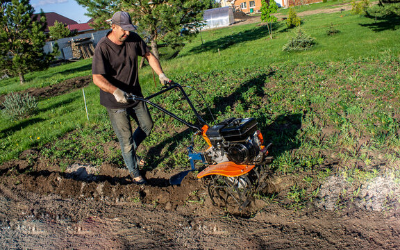 Male in the spring plows the earth in working clothes with a motoblock