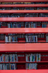 A slight topside, frontal view of rows of tall red metal bookshelves with books