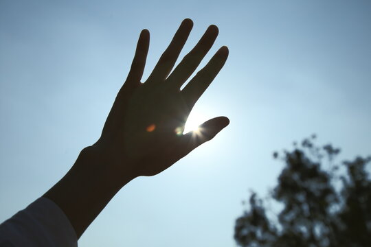 Backlight cropped hand covering sun. Low-angle view. Lens flare